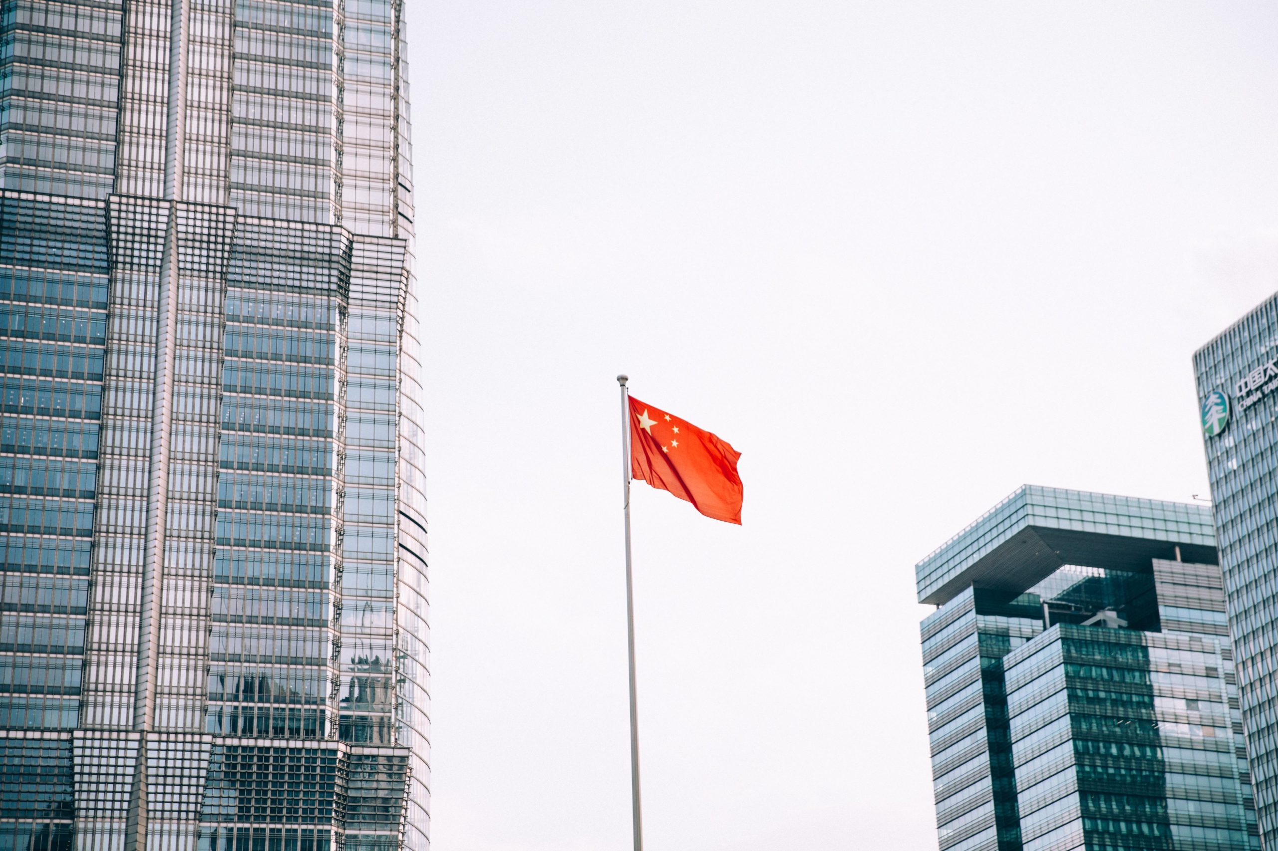 Picture showing the flag of china flying in the distance, among modern high-rise buildings.