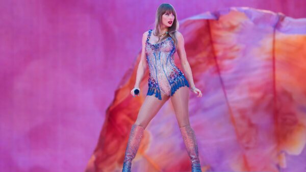 Taylor Swift poses in front of a gauzy purple and orange fan at the beginning of her 'Eras Tour.'