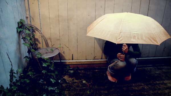 Person on garden decking with an umbrella covering their entire face, sitting as if anxious and unhappy.