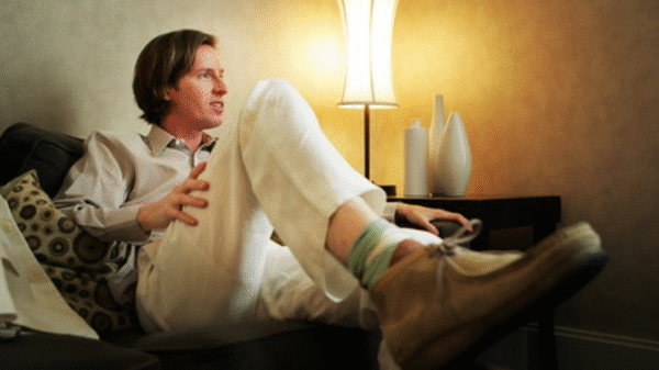 An image of director Wes Anderson seated on a sofa