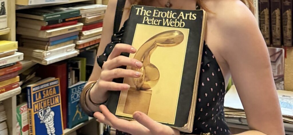 a girl holding a book titled "the erotic arts"