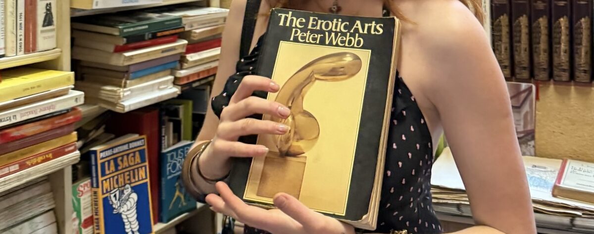 a girl holding a book titled "the erotic arts"