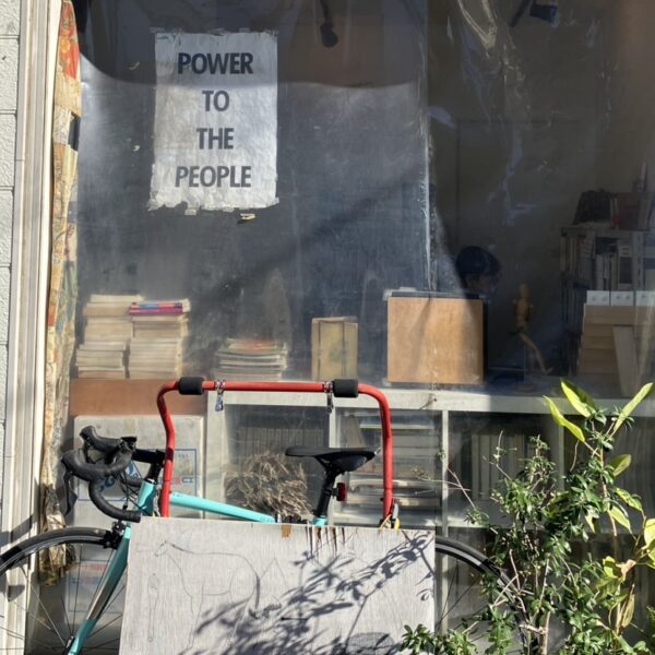 Exterior of Tanaka Hon'ya, a second-hand bookstore in Nezu, Tokyo, with plants and a wooden signboard outside.