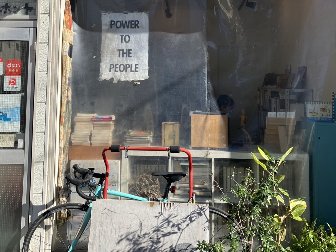 Exterior of Tanaka Hon'ya, a second-hand bookstore in Nezu, Tokyo, with plants and a wooden signboard outside.